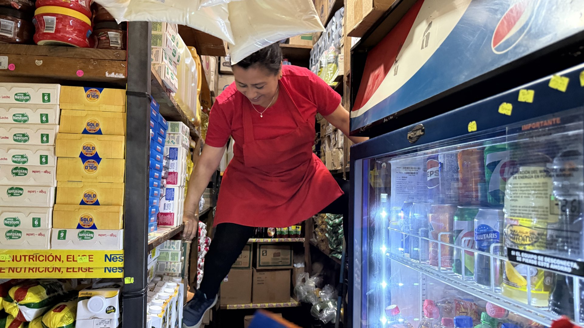 Empleada de Abarrotería Hellen reabasteciendo producto en los estantes altos